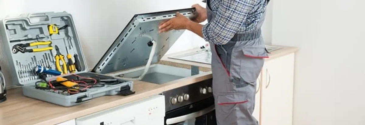 Cooktop repair technician lifting a built-in stovetop for service in Evansville, IN