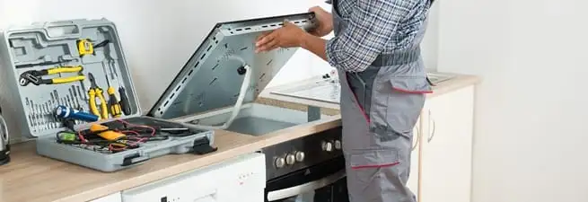 Cooktop repair technician lifting a built-in stovetop for service in Evansville, IN