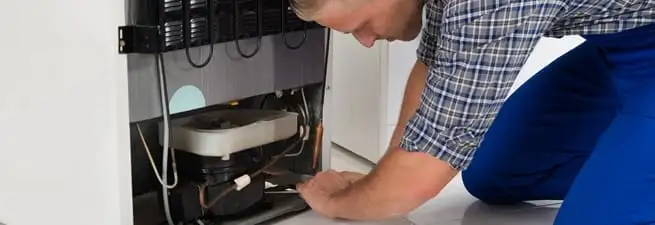 Refrigerator repair technician servicing the compressor and condenser area in Evansville, IN
