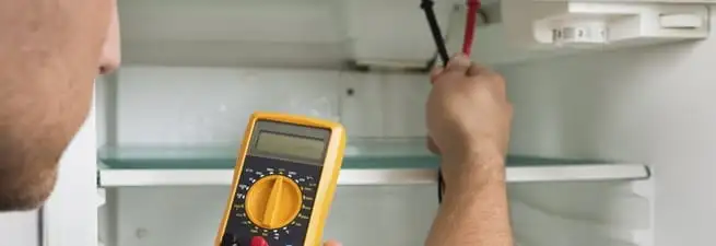 Refrigerator repair technician testing electrical components with a multimeter in Evansville, IN